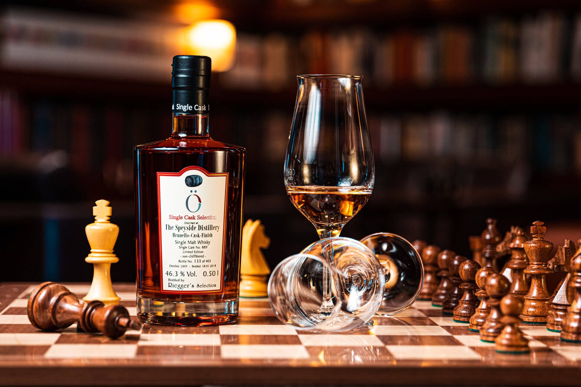 Whisky-Flasche steht neben zwei Gläsern auf einem Schachbrett