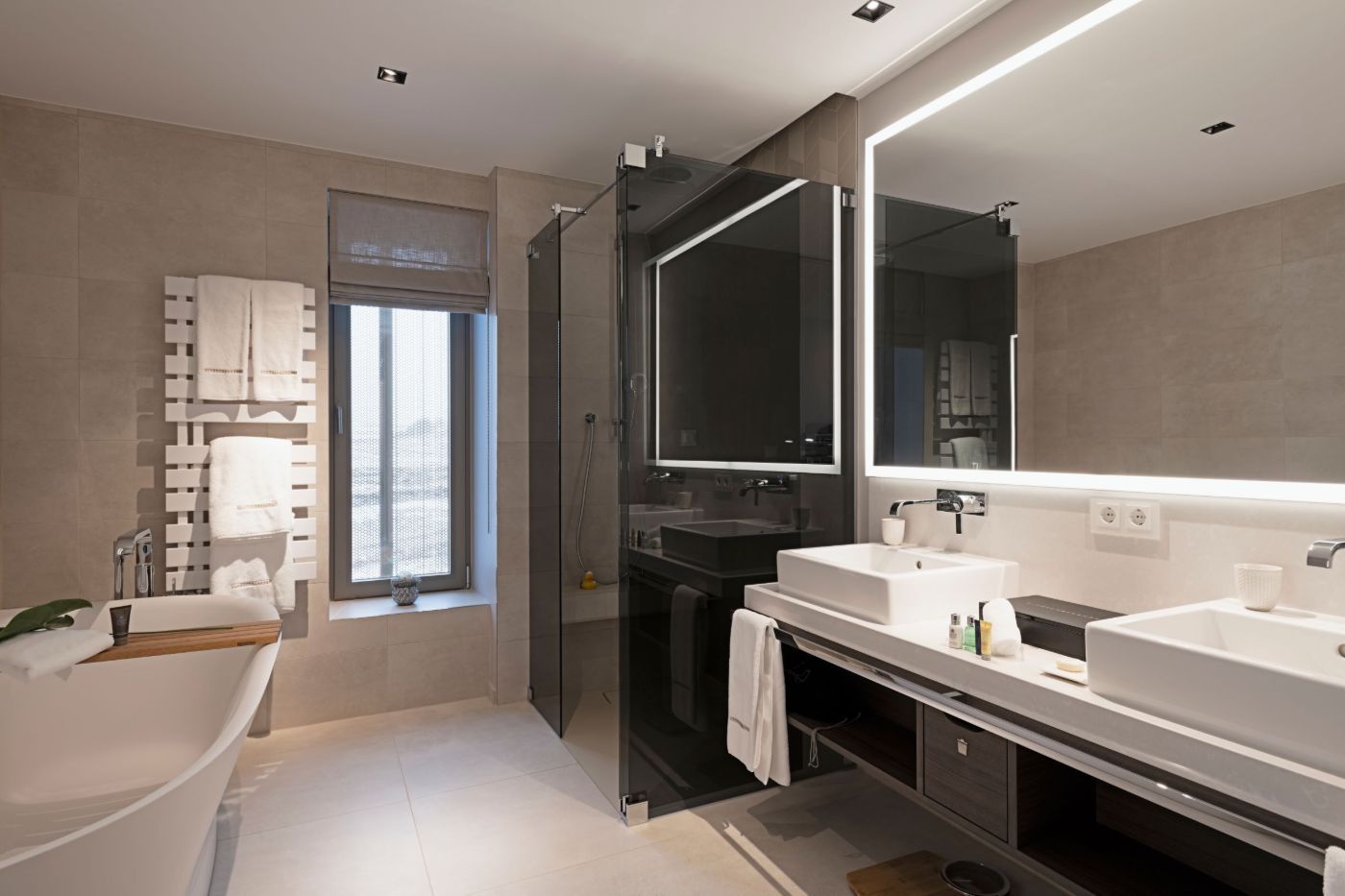 Großzügiges Badezimmer mit Badewanne, Dusche, zwei Waschbecken und einem großen, beleuchtetem Spiegel