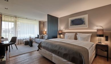 view on a queen size bed next to a lounge area with a couch and a side table in a 5 star hotel in the black forest