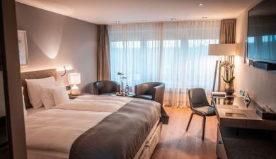 spacious queen size bed next to two armchairs on a window front