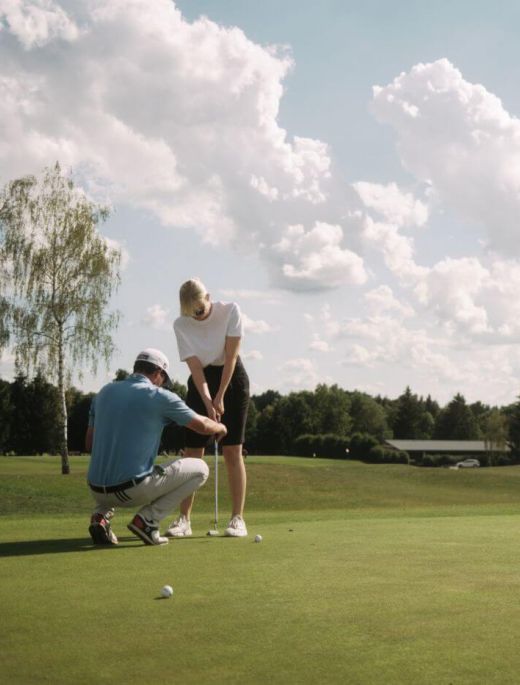Frau lernt von ihrem Trainer den Golfabschlag