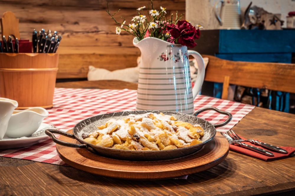 Eine Pfanne mit Kaiserschmarren bedeckt mit Puderzucker in der traditionell eingerichteten Öventhütte