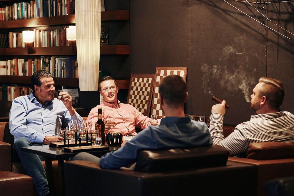 Vier Männer in der Smokerlounge rauchen Zigarren und trinken Whiskey