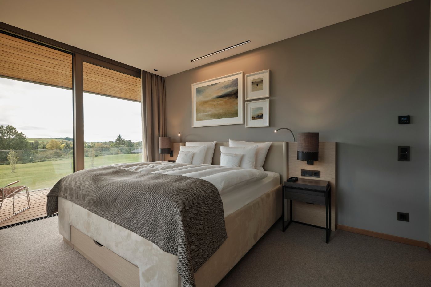Gemütliches Doppelbett neben einem großen Fenster mit Blick auf den Golfplatz