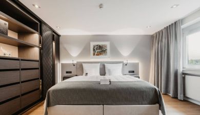 Bett neben einem Kleiderschrank aus dunklem Holz und indirekter Beleuchtung