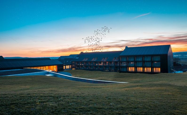 Blick auf die Außenfassade mit beleuchteten Zimmern des 5 Sterne Hotels im Schwarzwald in  der Abendröte