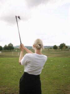 junge_frau_auf_unserem_golfplatz_nach_abschlag_haelt_die_den_schlaeger_noch_oberhlab_ihrer_linken_schulter