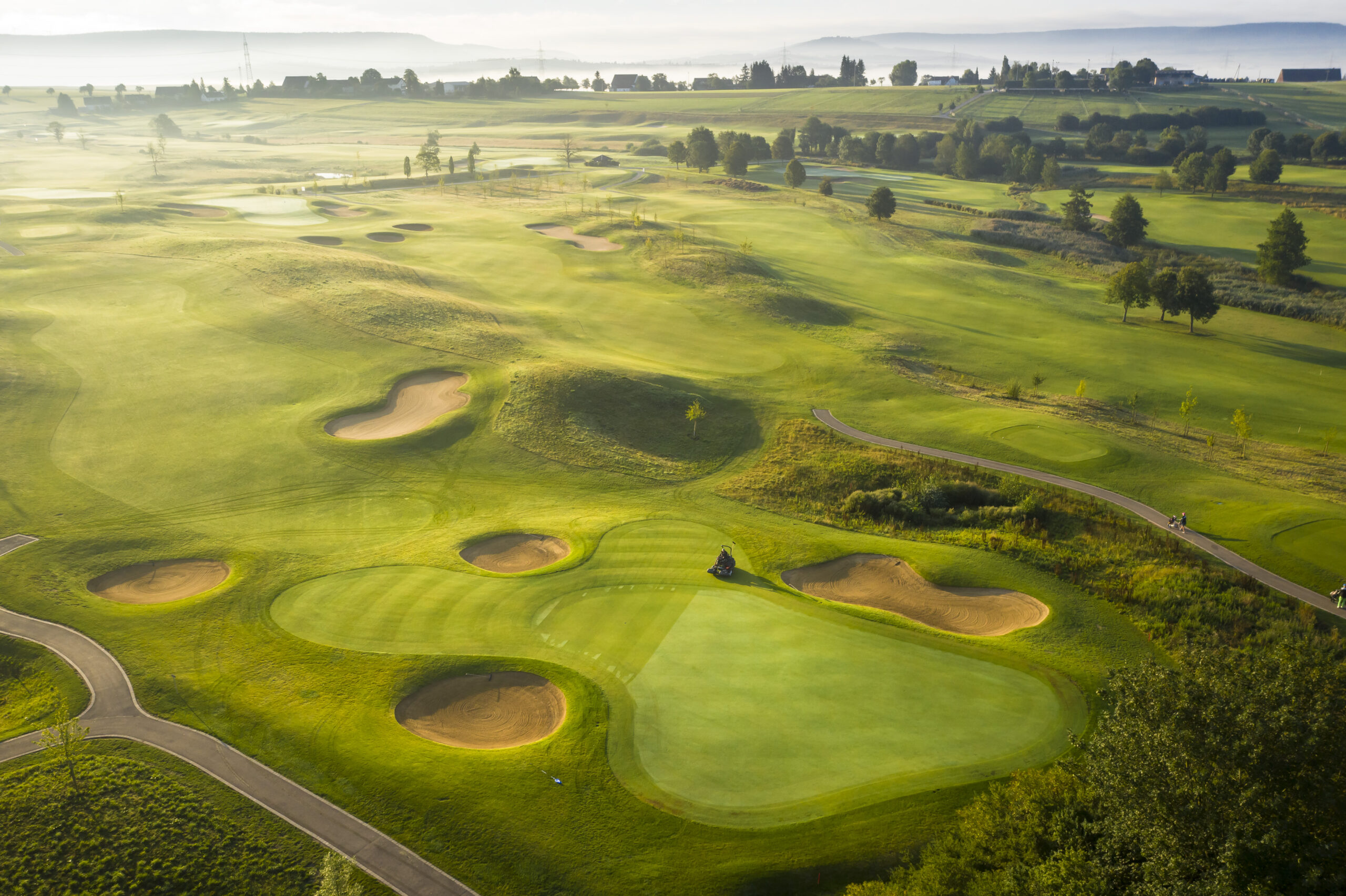 golfplatz-bei-schonem-wetter-aber-leicht-diesigem-himmel-von-oben-mit-drohne-fotografiert-sicht-auf-einige-sandbunker-und-kleine-baeume