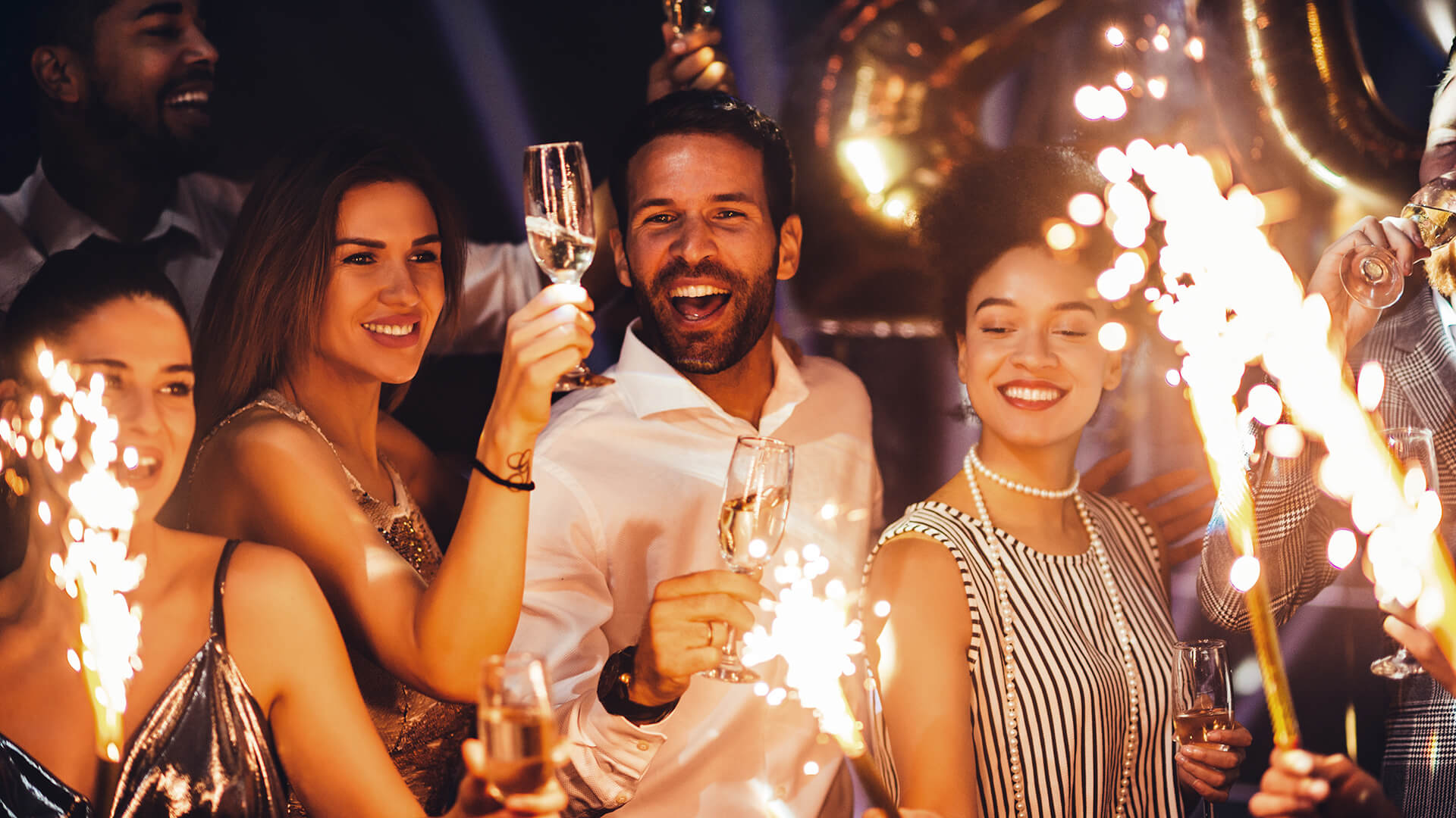 Mehrere Menschen feiern mit Wunderkerzen und Sekt
